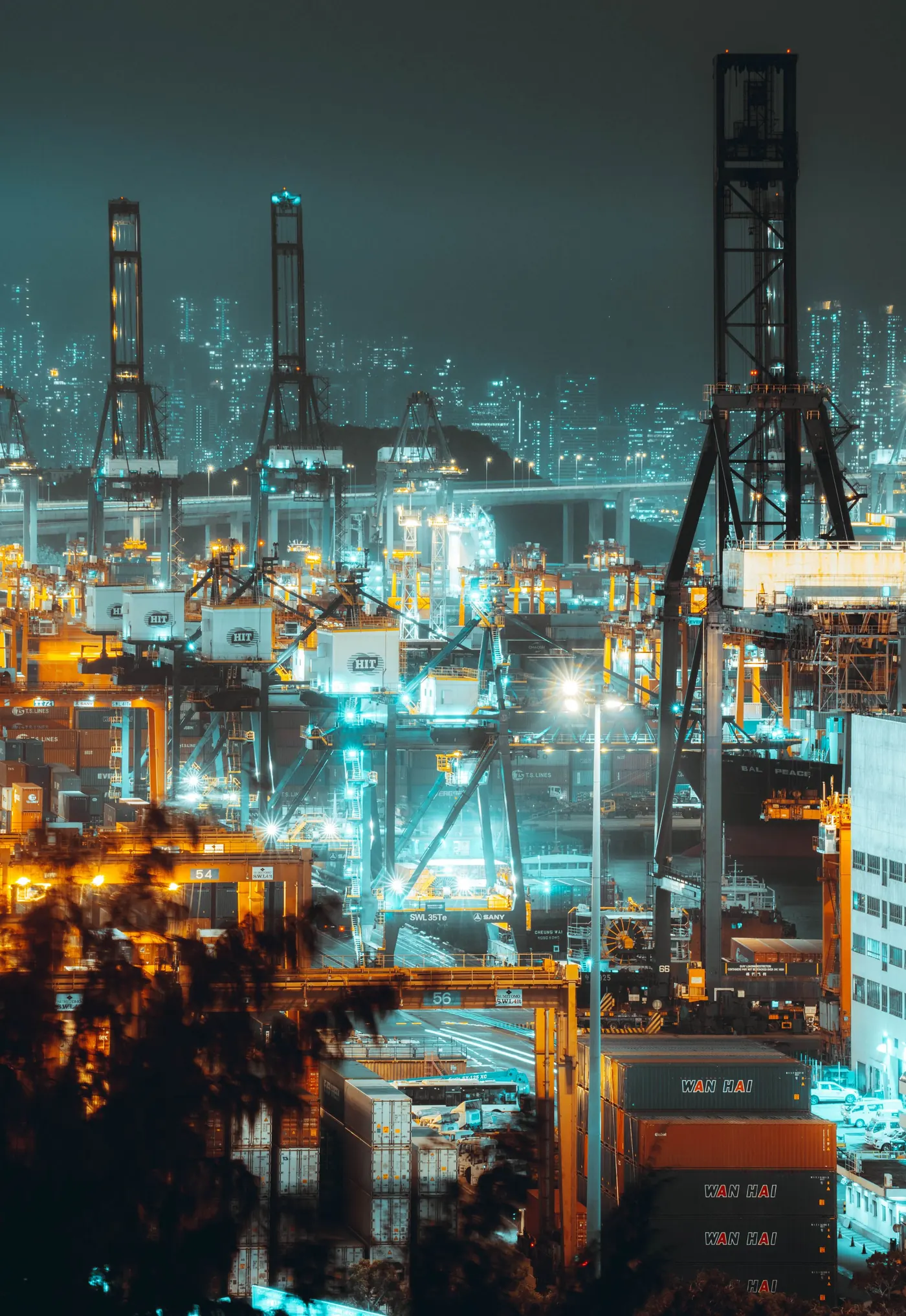 Nighttime aerial view of Hong Kong's bustling shipping port with illuminated cranes and containers