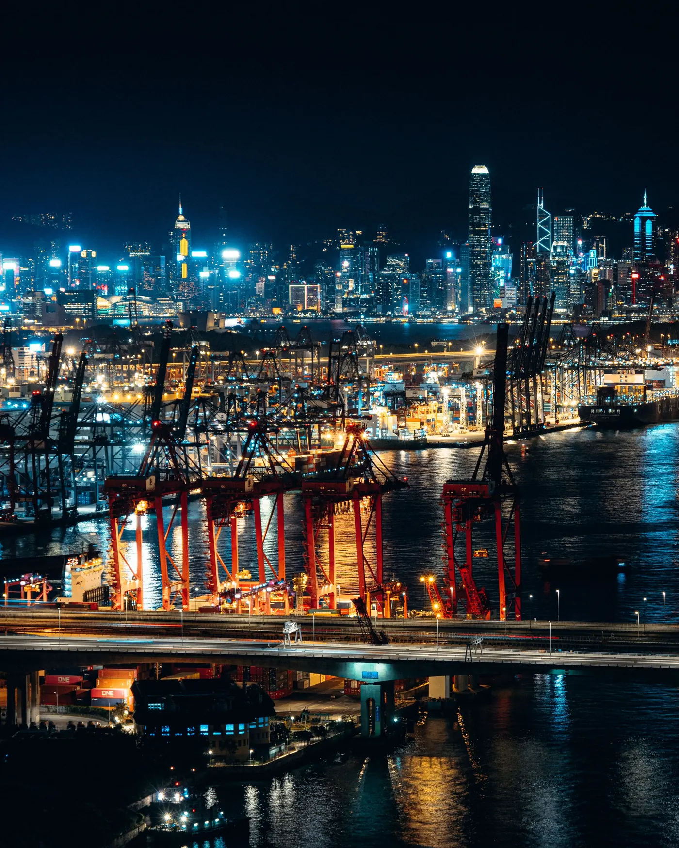 Night view of Hong Kong port with luminous cityscape backdrop showcasing cranes and skyscrapers